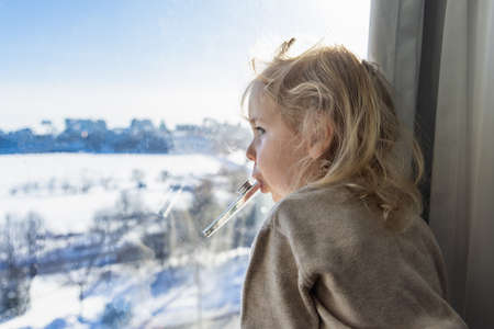 Closeup side view of a sweet three year old boy with wavy blonde hair looking out of a window over a rural snowy landscape scene. Copy space to left.の写真素材