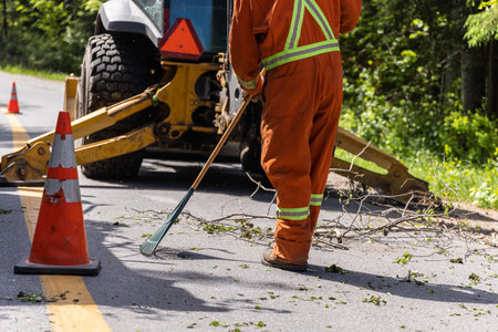 Closeup view as a worker is seen wearing high visibility clothes, using a rake to clear tree...