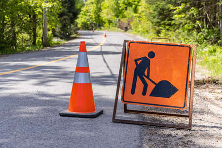 Close up view of a warning, beware of workforce in road sign and traffic cone on a highway. Blurry rural freeway and cones are seen in background.の写真素材