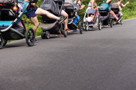 Group of parents performing cardio together in a nature environment, with their babies in strollers on a sunny day in the park dressed in summer clothesの写真素材