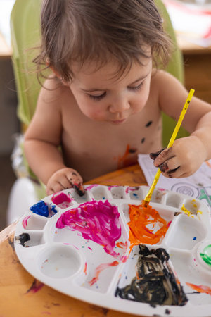 Young artist is focused on dipping her paintbrush into a colorful and messy paint palette. Selective focusの写真素材