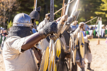 Medieval reenactors wearing chainmail armor and holding swords and shields are lined up, participating in a simulated battleの写真素材