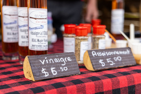 Bottles of maple syrup vinegar and jars of seasoning sitting on a red and black checkered tablecloth with wooden price signs. Selective focusの写真素材