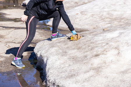 Volunteer is collecting trash from the melting snow in the mountains wearing gloves. Selective focus