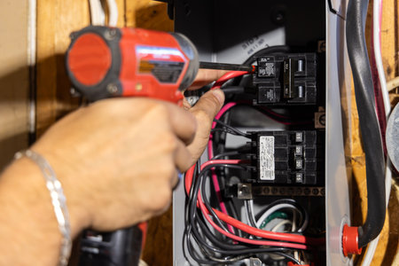 Electrician is installing a new circuit breaker in a residential electrical panel using a power...
