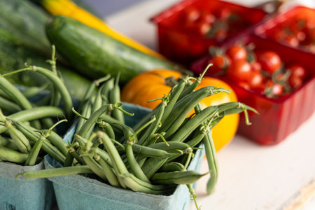 Freshly picked green beans are overflowing from baskets with other vegetables blurred in the...