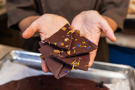 Chocolatier presenting a selection of artisanal chocolate pieces adorned with edible flowers and...