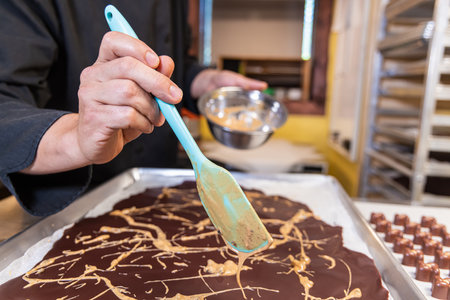 Chocolatier is spreading cream over a layer of dark chocolate on a baking sheet to make a delicious dessert. Selective focusの写真素材