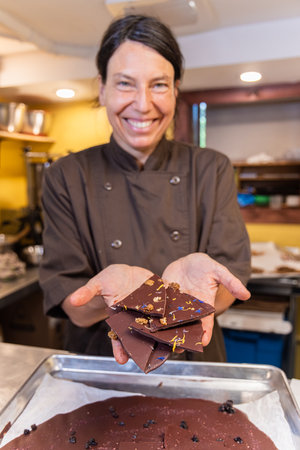 Chocolatier woman smiling and holding pieces of dark chocolate with nuts and flowers in her hands. Selective focusの写真素材