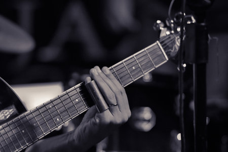 Details of an acoustic guitar, with emphasis on the hand of the blues guitarist with a slide on the pinky finger. Black and white photo. Selective focus.の写真素材