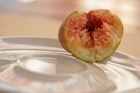 Half a fig, a juicy ripe tropical fruit lies on a white plate. Space for text on the left. Beautiful...