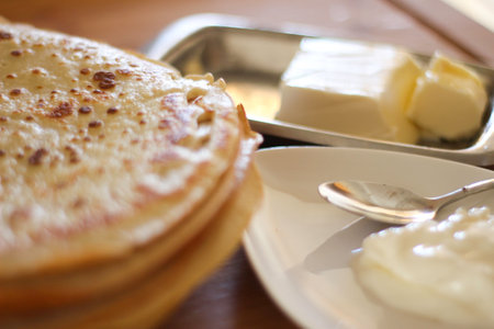 Maslenitsa. A stack of yeast millet pancakes with a stream of honey on a background of butter, a teaspoon of sour cream in a white dish. Defocusの写真素材