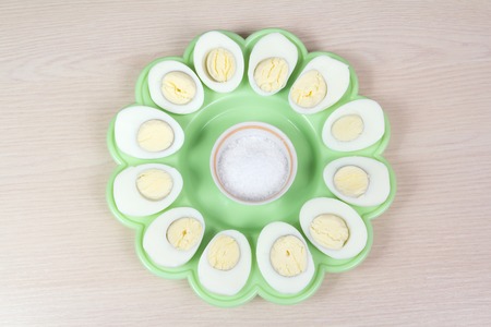 slices of boiled chicken eggs on a green plate with salt in the middleの写真素材