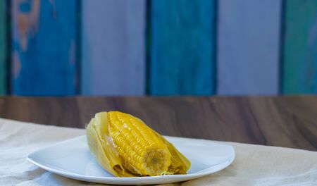 boiled green corn cob with butter and straw on wooden table with blue aged wood backgroundの写真素材