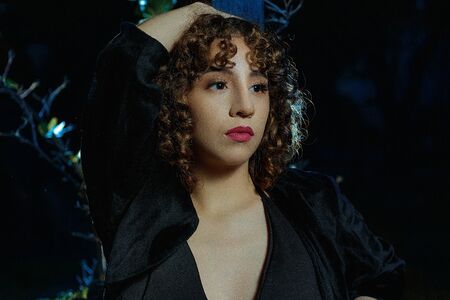 Young girl with curly brown hair, Caucasian skin, red lipstick, black suit and white and black checkered skirt, strolling through the square in the late afternoon and early evening.の写真素材