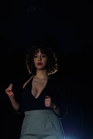 Young girl with curly brown hair, Caucasian skin, red lipstick, black suit and white and black checkered skirt, strolling through the square in the late afternoon and early evening.の写真素材