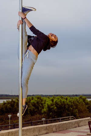 Alternative-looking woman practicing Poledance street on poles in city parks