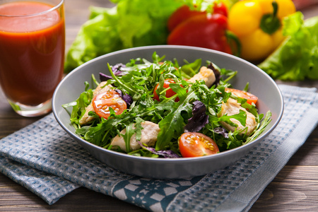 Fresh salad with chicken, tomatoes, arugula, mesclun, basil and orange juice on a cloth napkin, on wooden table. Healthy food.の写真素材