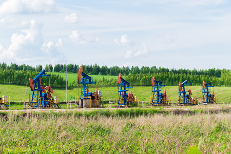 working oil pumps on the ground among the green fieldsの写真素材
