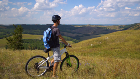 Young man on a bicycle among the green hill against a sky with cloudsの写真素材