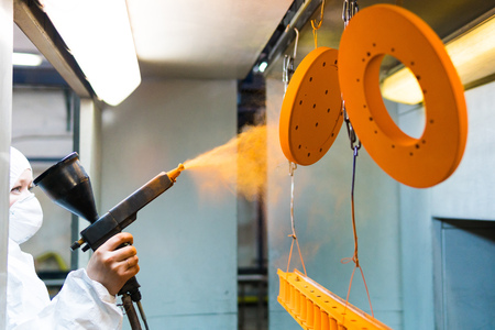 Powder coating of metal parts. A woman in a protective suit sprays powder paint from a gun on metal productsの写真素材