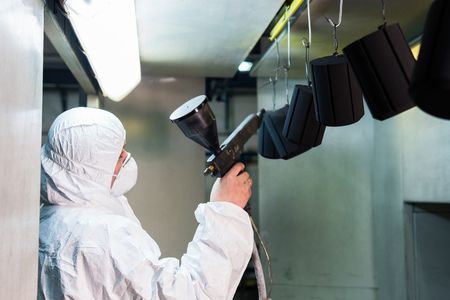 Powder coating of metal parts. A man in a protective suit sprays powder paint from a gun on metal productsの写真素材