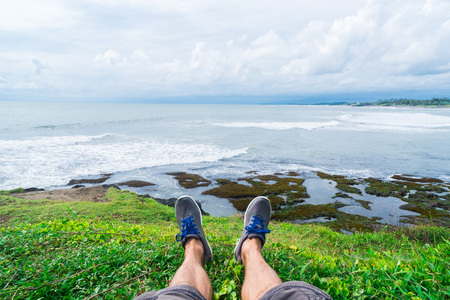 first person view. The man traveler sits on the edge of the cliff with his legs dangling. At the...