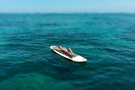 A beautiful young woman relaxes on a SUP board in the sea near the island. Drone shotの写真素材