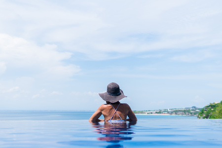 Attractive woman in bikini and with grey hat is relaxing in an infinity poolの写真素材