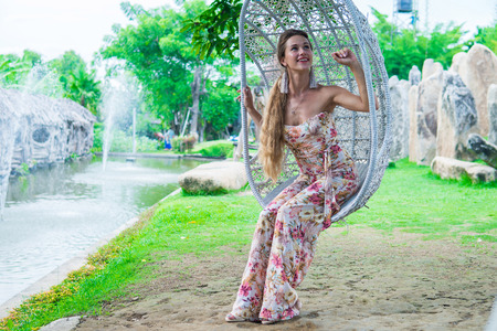 Beautiful brunette in dress swinging on a swing over the water in the Park in Sunny dayの写真素材