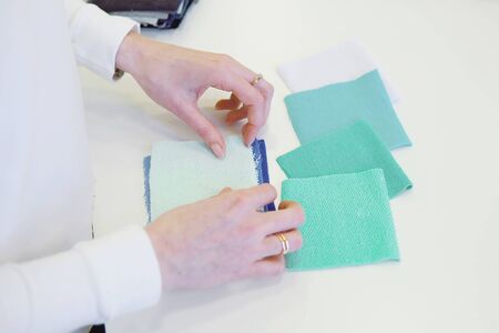 Young female dressmaker choosing material from catalogue in studio. Tailor looking through fabrics while standing in a sewing workshop. Close upの写真素材