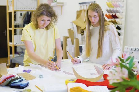 Two female fashion designers working together at workplace at workshop for sewing clothes,...