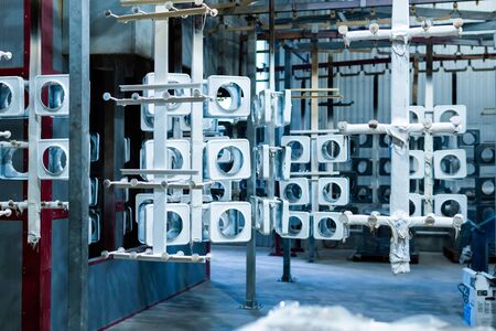 line for painting metal products in white color coating. Square metal products with a round hole hang on mounts after powder paintingの写真素材