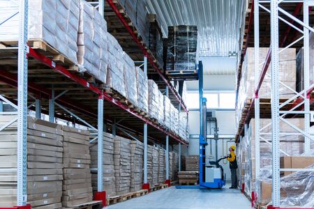 warehouse worker driver in uniform delivery and loading cardboxes by forklift stacker loaderの写真素材
