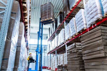 warehouse worker driver in uniform delivery and loading cardboxes by forklift stacker loaderの写真素材