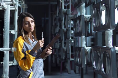 A young pretty white woman works in the paint shop of the plant, she checks the unpainted metall products and making record in check list.の写真素材