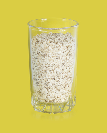 Rolled oats (oat flakes) in a glass on a yellow background.の写真素材