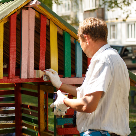 Summer work. A man is staining a toy home with a brushの写真素材