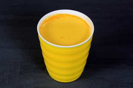 Golden turmeric milk in a yellow cup on a gray background