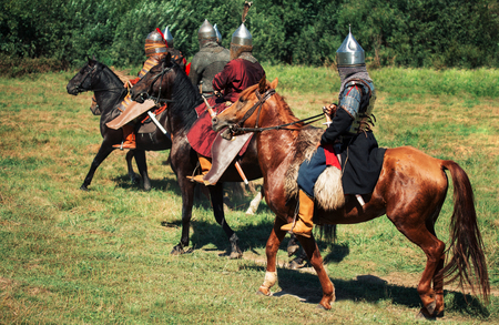Group of ancient equestrians in historical costumes are reconstructed. The medieval armored knights are on the horses. The historical reenactors are in the summer fieldの写真素材