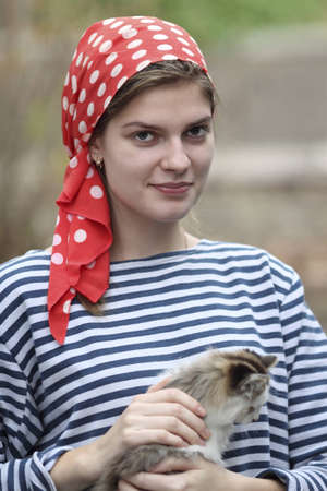 beautiful girl in a red kerchief and a striped t-shirt playing with a kittenの写真素材