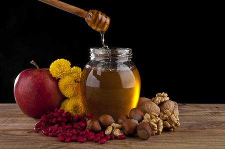 jar of honey, red Apple, nuts and yellow flowers on a black backgroundの写真素材