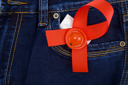 condom and red ribbon in the pocket of blue jeansの写真素材
