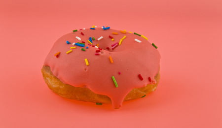 donut with pink icing on a pink backgroundの写真素材