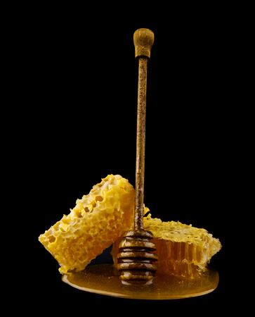 Honeycomb with honey spoon isolated on black background, bee natural ingredients conceptの写真素材
