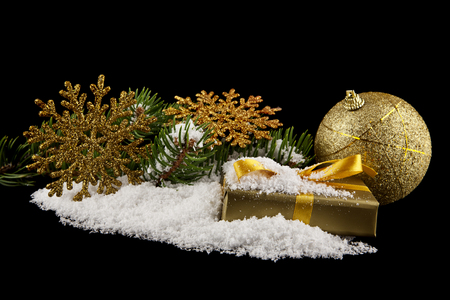 green branch of a tree in the snow with a golden ball, snowflakes and a gift isolated on a black backgroundの写真素材