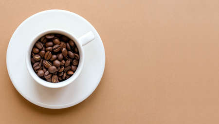A cup of coffee with a saucer and coffee beans on a brown solid background with space for textの写真素材
