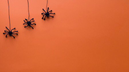 Black toy spiders descend on cobwebs on. Orange background for Halloweenの写真素材