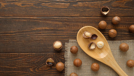 Macadamia nuts and wooden spoon. Whole and open nuts, shell fragments on a wooden brown backgroundの写真素材
