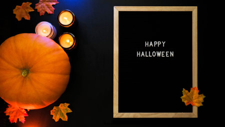 Pumpkin, burning candles, autumn leaves and the inscription Happy Halloween in a wooden frame on a black backgroundの写真素材